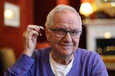 A man holding up a hearing aid and smiling in Anchorage, AK