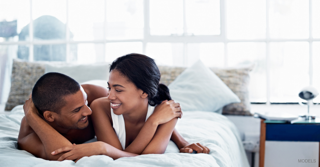 Young man and woman lying in bed on their stomachs smiling and snuggling