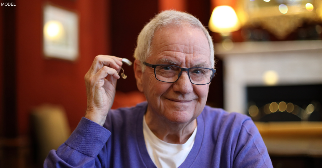 A man holding up a hearing aid and smiling in Anchorage, AK